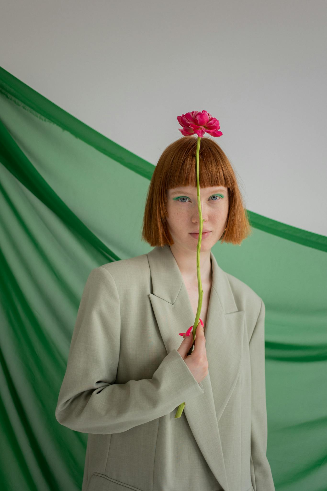 An artistic portrait of a woman holding a flower in a minimalist studio setting, featuring bold colors and stylish composition.