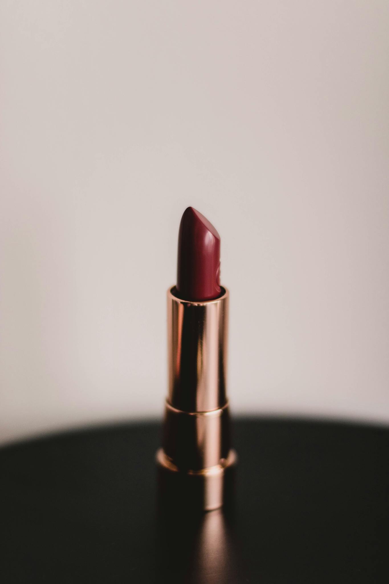 Close-up of a burgundy lipstick in a gold tube on a neutral background, exuding elegance.