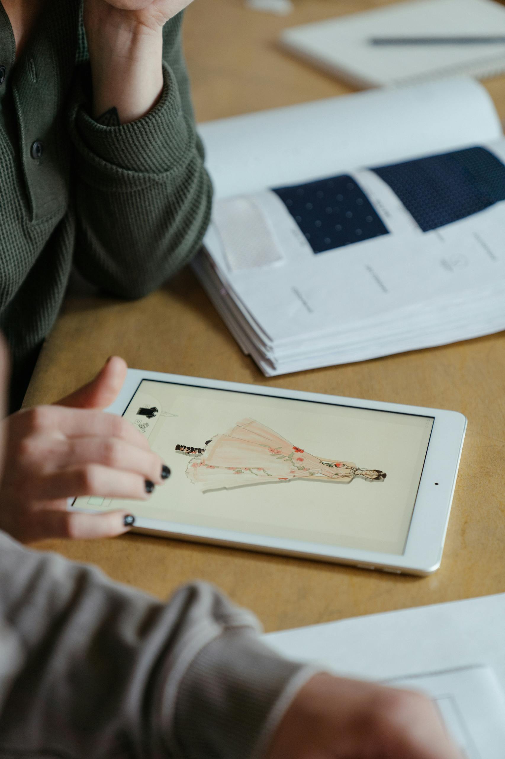 Close-up of fashion designer sketching clothing designs on a tablet at a workshop table.