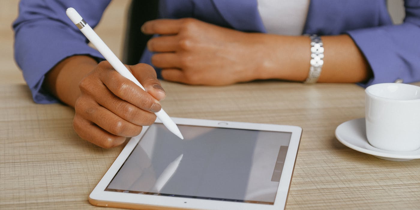 African American woman using a stylus on a tablet at a desk, with coffee nearby.