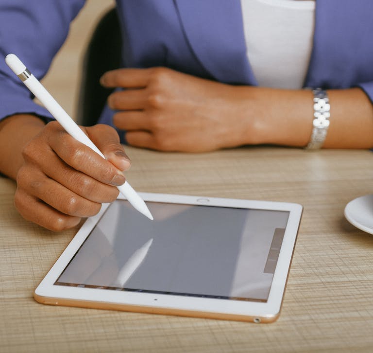 African American woman using a stylus on a tablet at a desk, with coffee nearby.