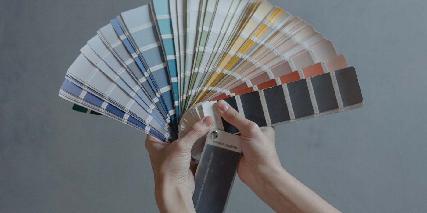 Hands displaying a fan of paint color swatches against a gray wall, ideal for home renovation projects.