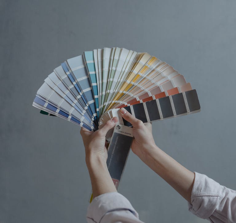 Hands displaying a fan of paint color swatches against a gray wall, ideal for home renovation projects.