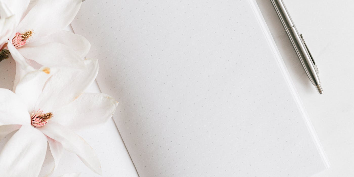 Top view of a blank notebook with magnolias and a silver pen, ideal for notes or journaling.