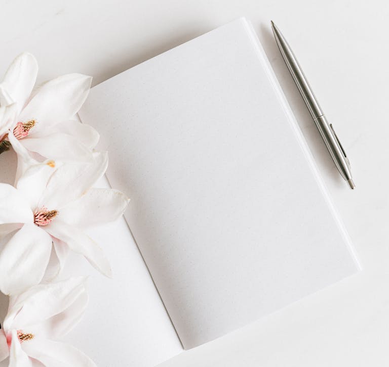 Top view of a blank notebook with magnolias and a silver pen, ideal for notes or journaling.